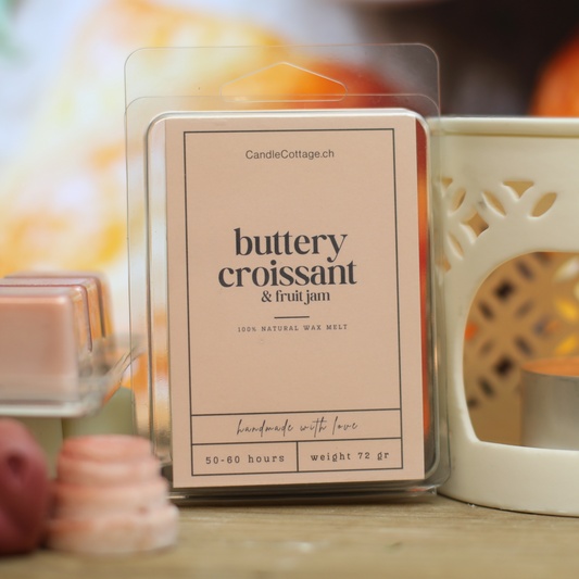 Buttery croissant and fruit jam wax melts packaging on wooden table with candle holder.