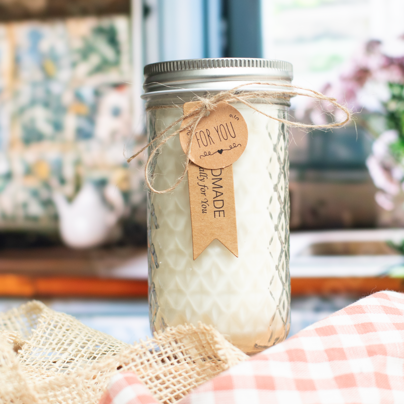 Ms. COTTI Lililee scent candle in a glass jar with a rustic label, placed on a checkered cloth, evoking a cottage charm.